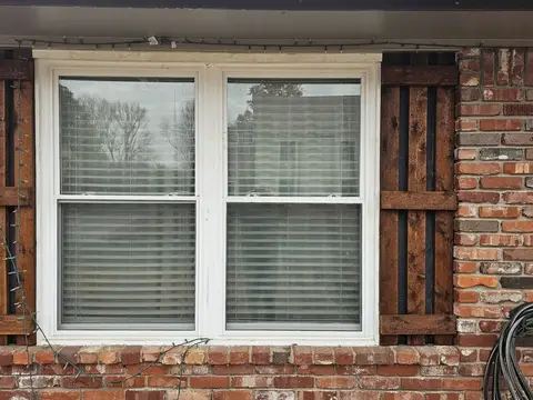 Two new white double-hung windows with brown shutters on a brick home