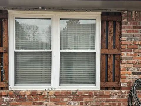 New white double-hung window between brown shutters on a brick wall