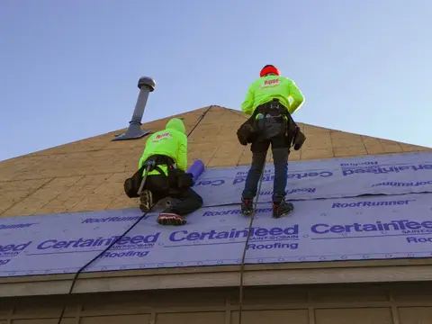 Two roofers laying synthetic underlayment across a roof plane