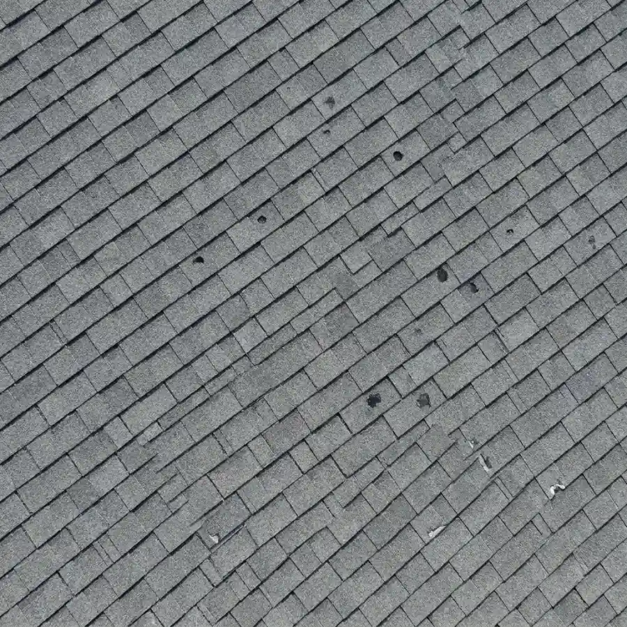 Close-up photo of an asphalt shingle showing starburst cracks radiating from a central hail impact point.