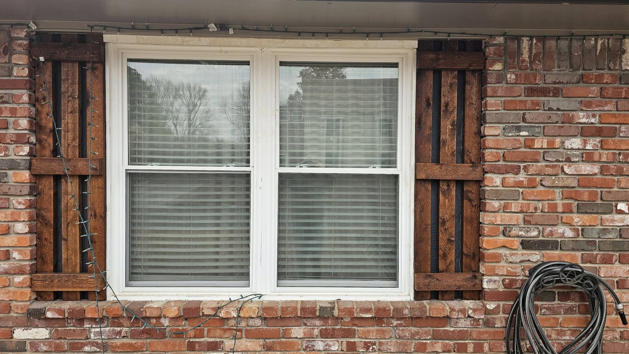 A window with wooden shutters and Christmas lights on a brick house.