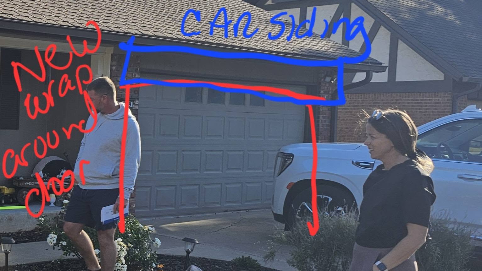 A man and woman stand in front of a garage door with red and blue markings indicating construction.