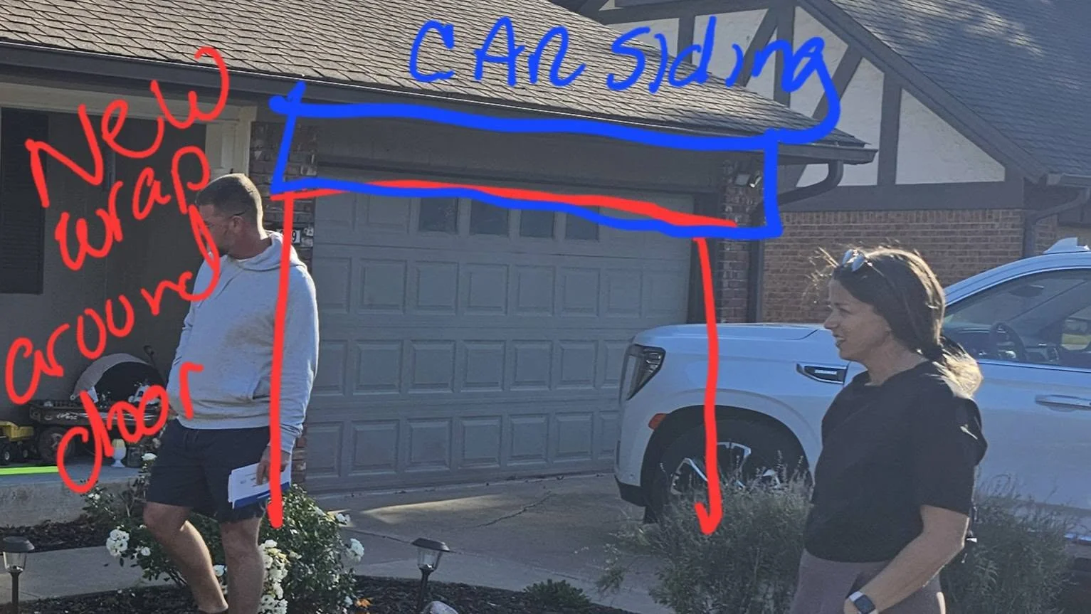 A man and woman stand in front of a garage door with red and blue markings indicating construction.