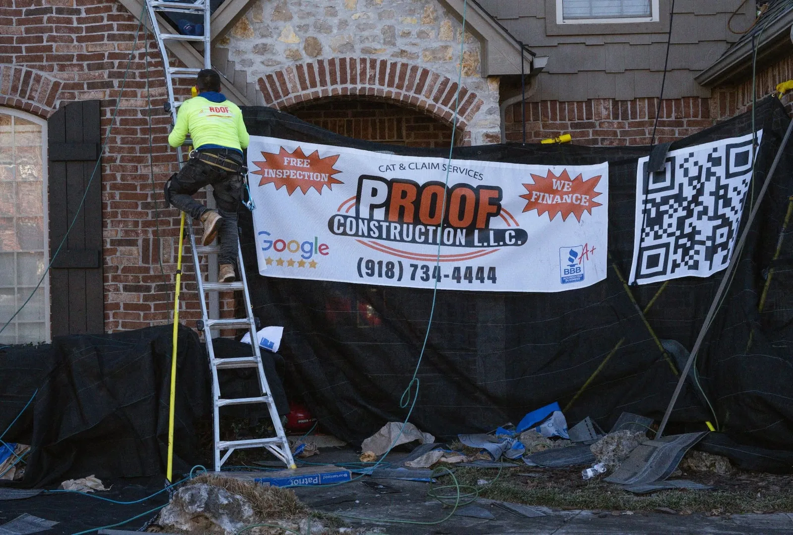 A roofer climbs a ladder in front of a banner for Proof Construction LLC.