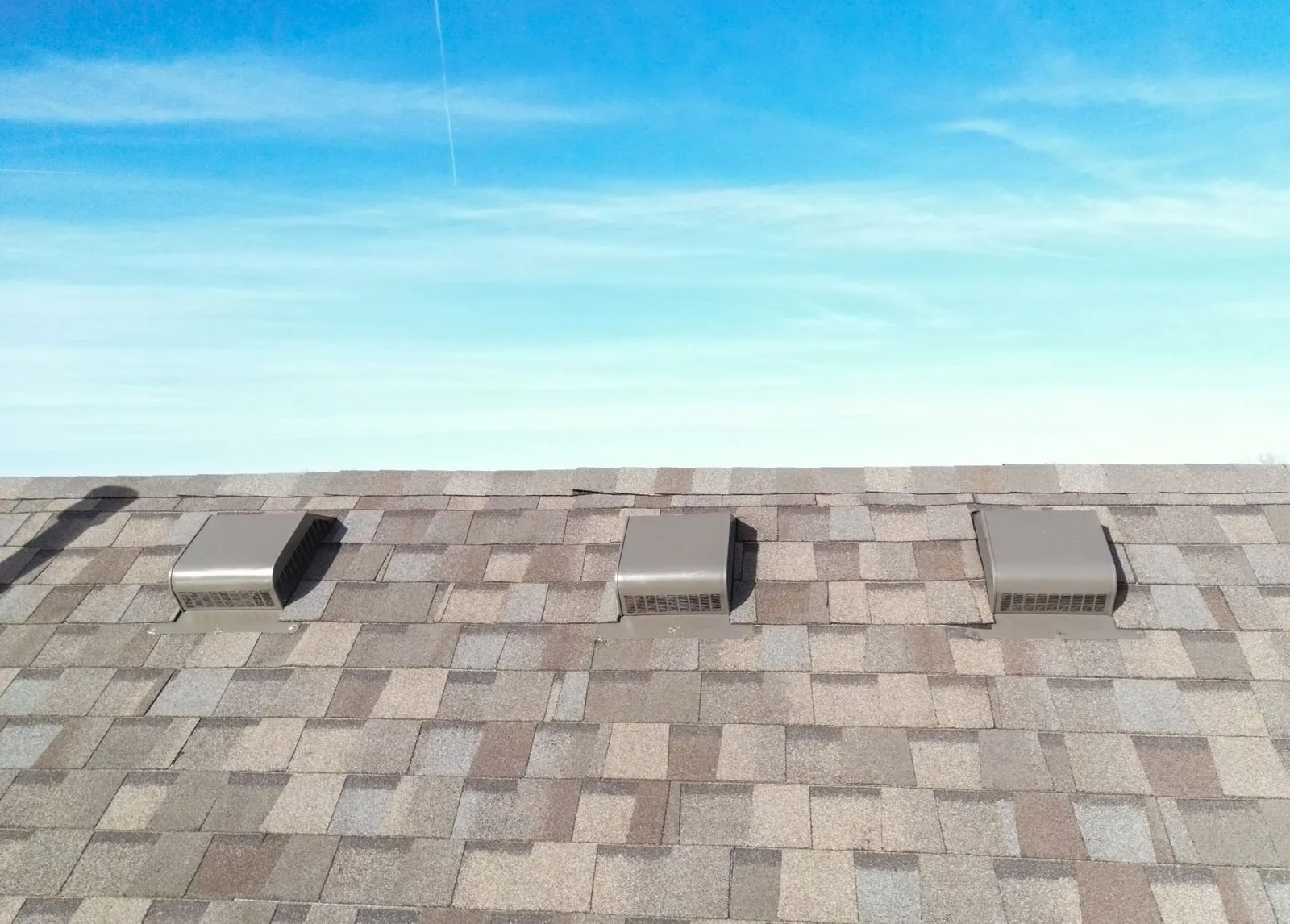 Three roof vents are visible on a shingled roof under a bright blue sky.