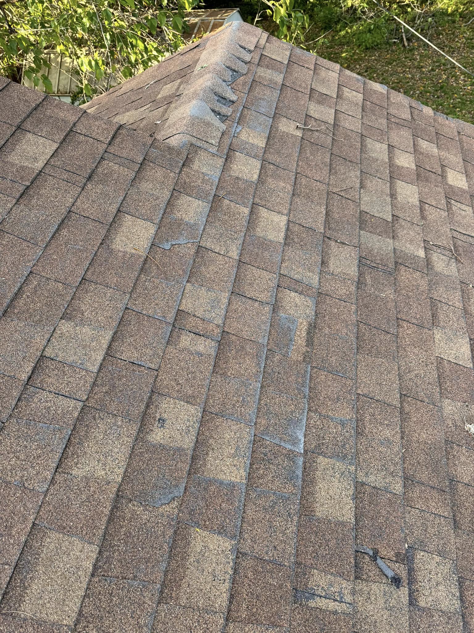 A damaged asphalt shingle roof is shown from an aerial perspective.
