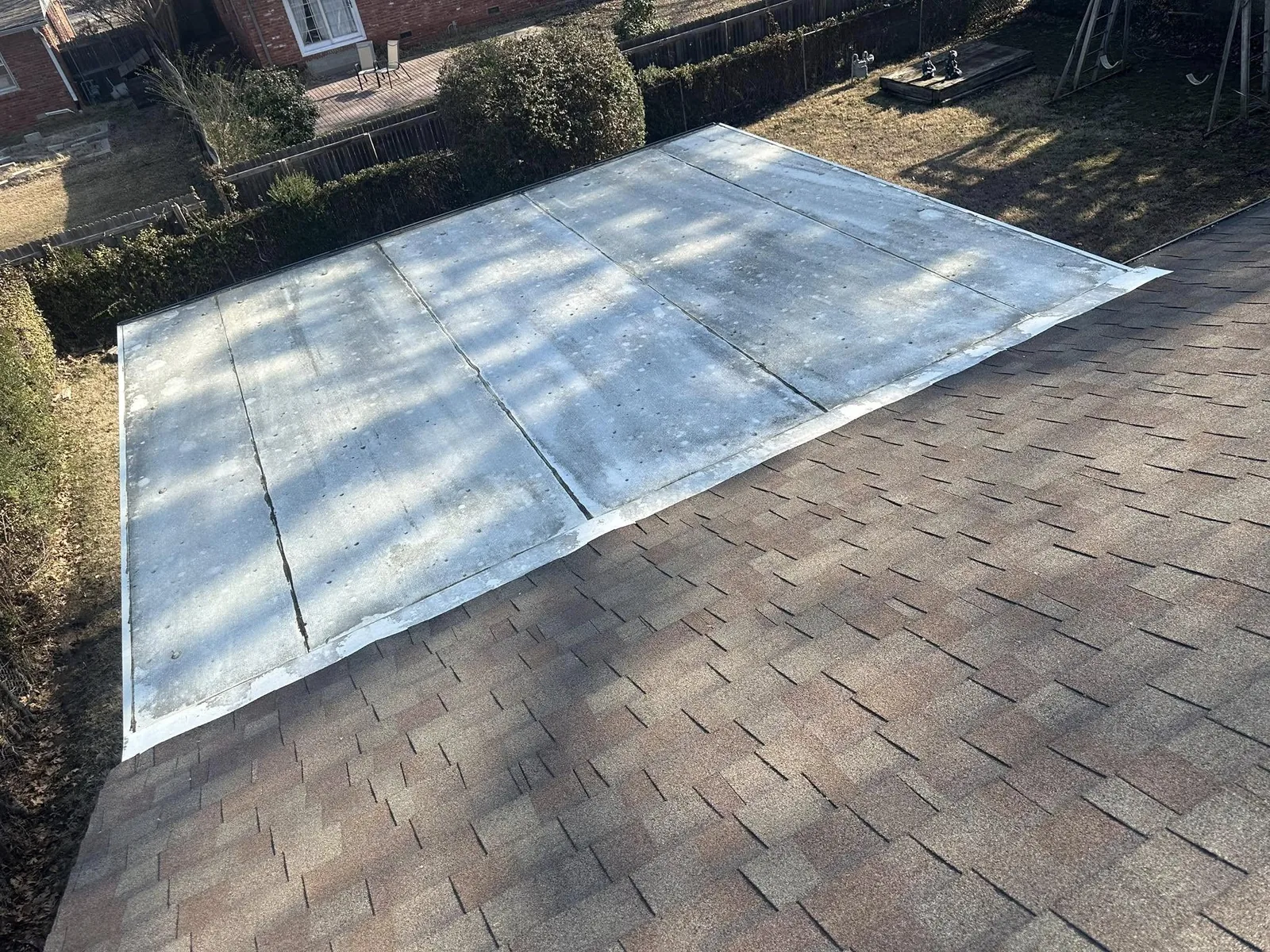 A flat roof section is installed over a sloped shingle roof in a backyard.