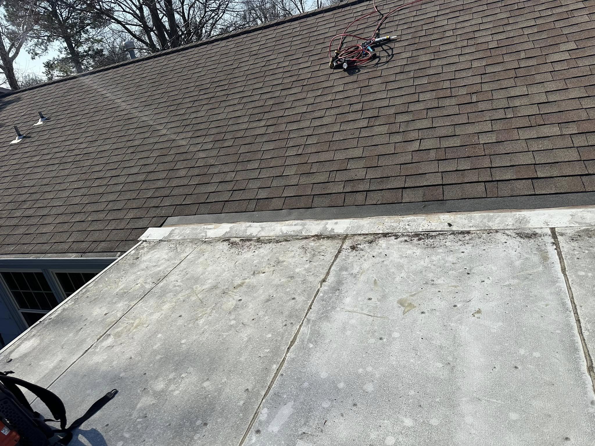 A rooftop with shingles and a flat section, featuring some equipment.