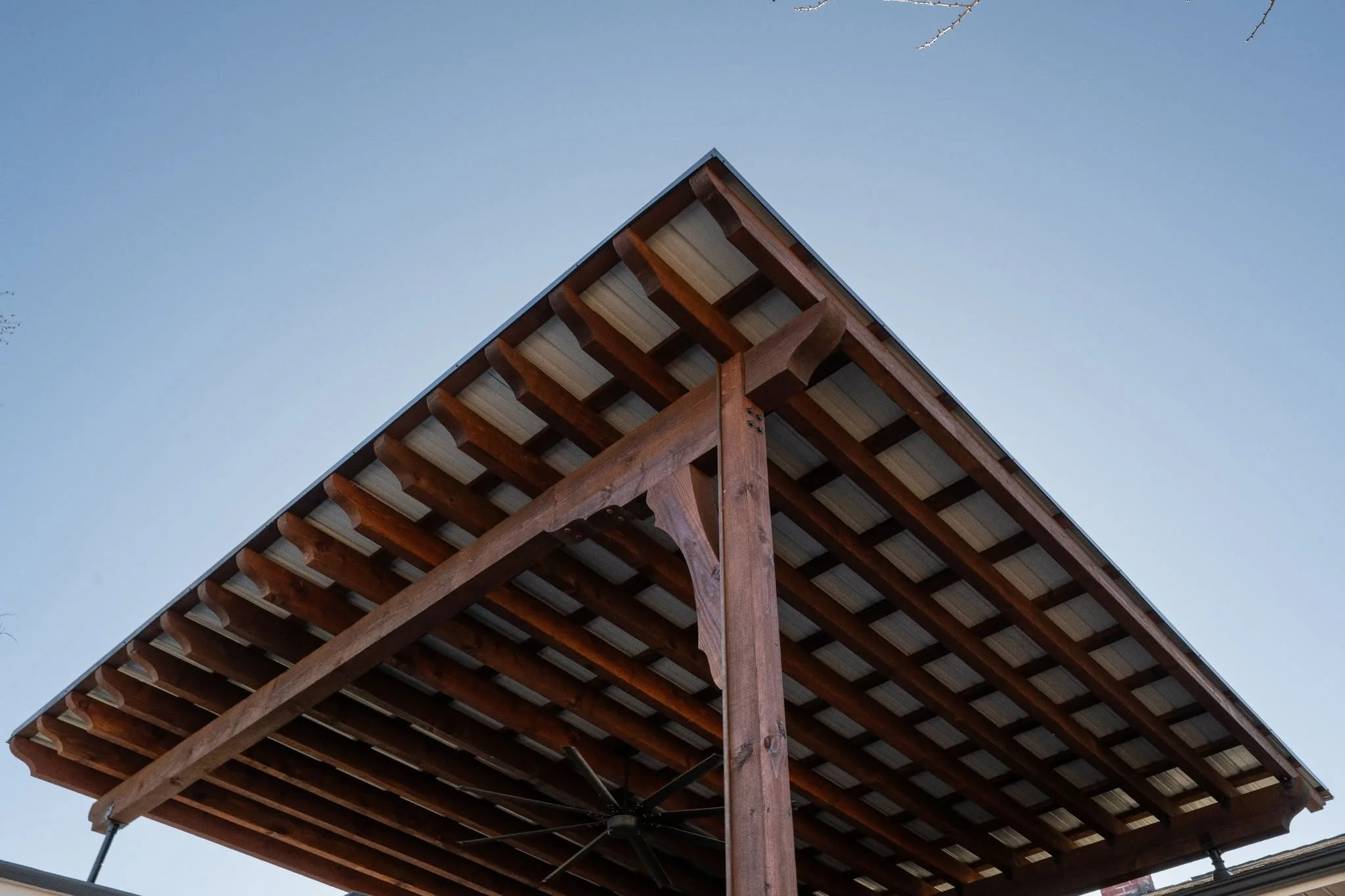 A wooden pergola with a metal roof is shown against a clear blue sky.