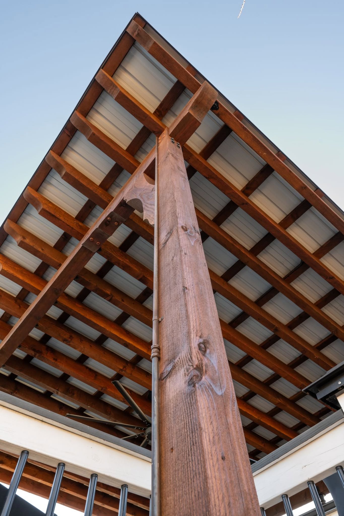 A wooden beam supports a metal roof structure against a clear sky.