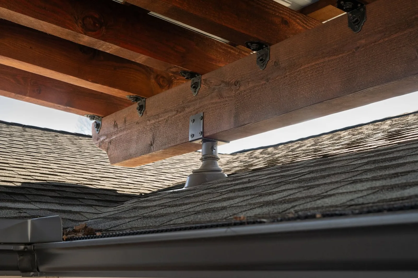 A wooden beam is supported by a metal bracket on a shingled roof.