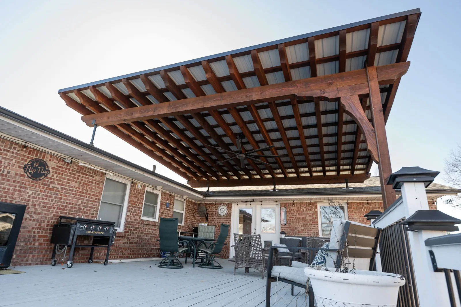 A covered patio with furniture and a grill on a deck attached to a brick house.