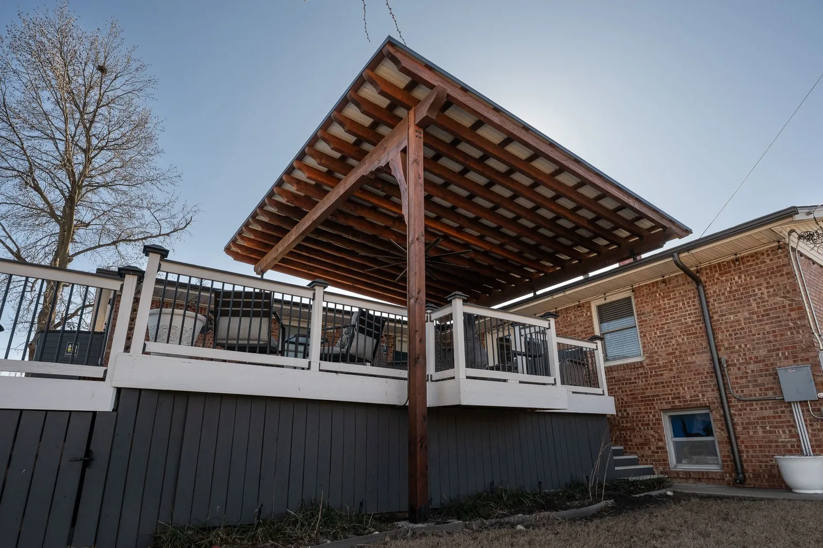 A wooden deck with a covered roof is attached to a brick house.