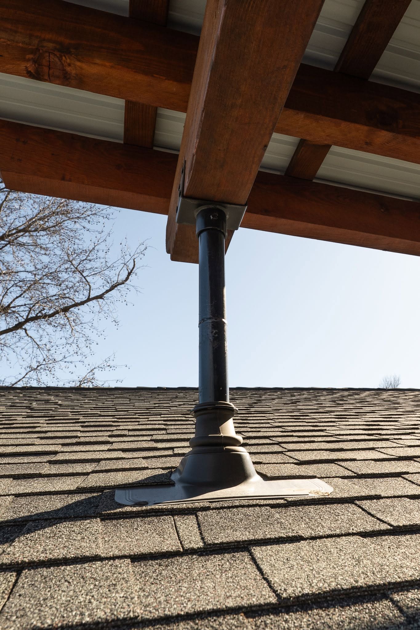 A dark metal support post holds up a wooden roof structure on a shingled roof.