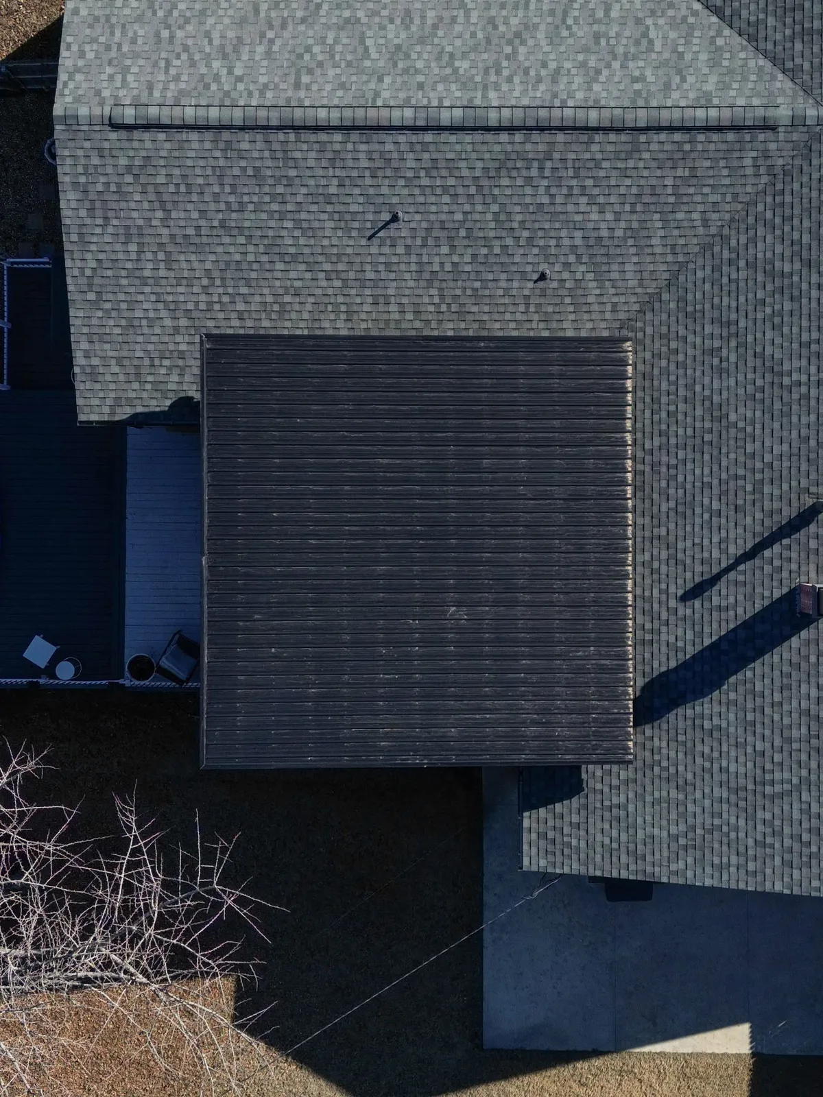 An aerial view shows a dark, flat-roofed addition attached to a grey, shingled house.