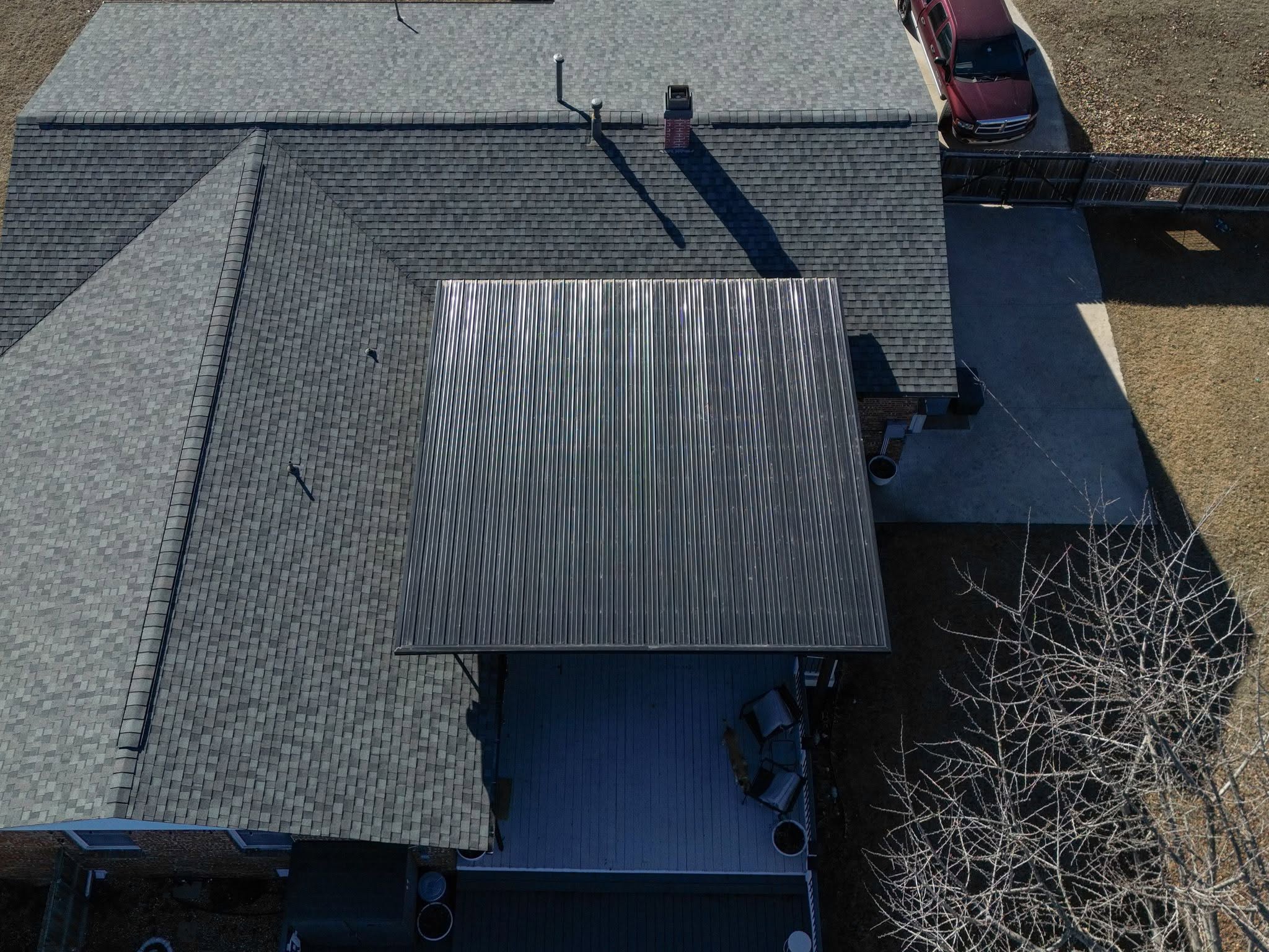 An aerial view shows a house with a metal roof extension over a deck, a car, and a fence.