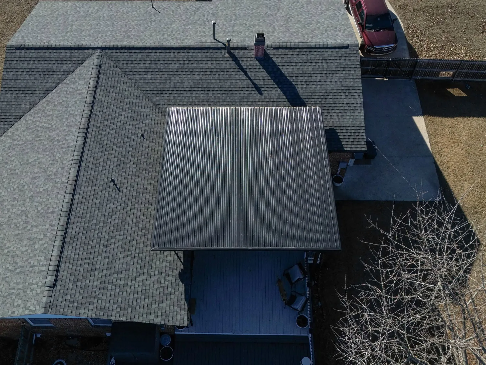 An aerial view shows a house with a metal roof extension over a deck, a car, and a fence.