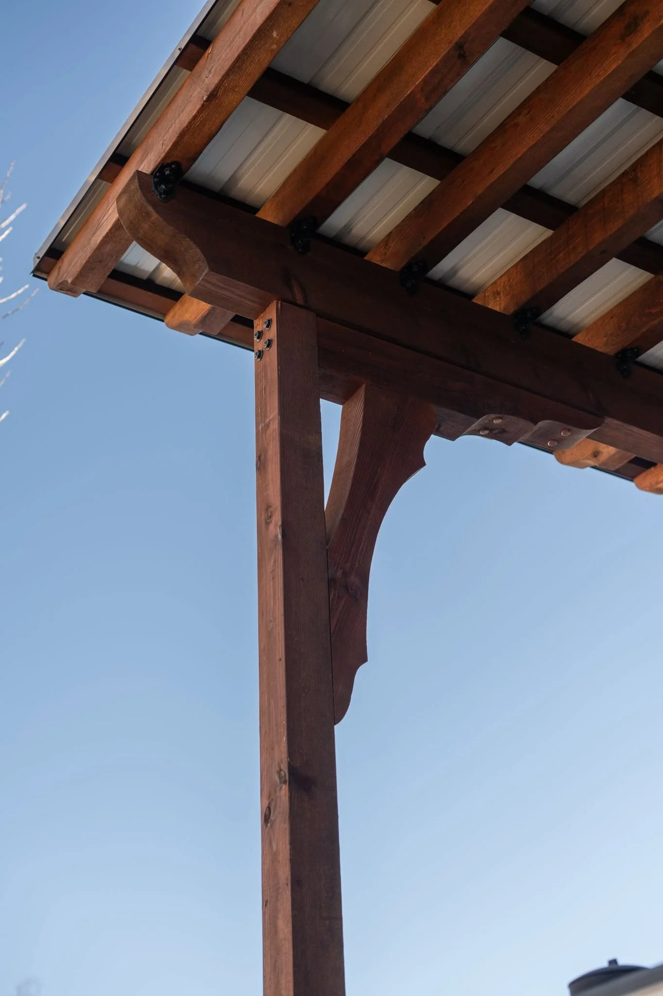 A wooden pergola with a metal roof is shown against a clear blue sky.