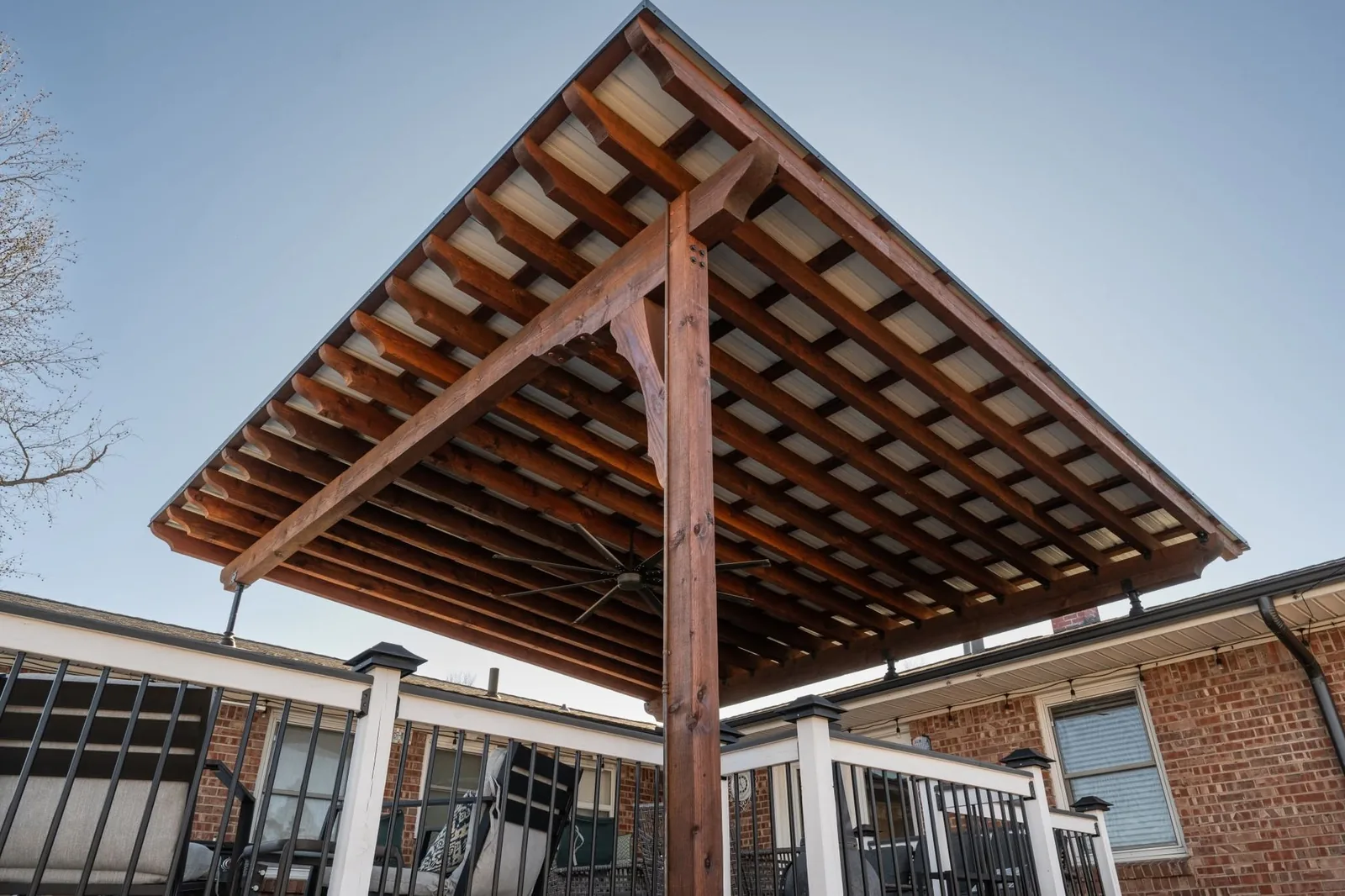A wooden pergola with a metal roof covers a deck with outdoor furniture.