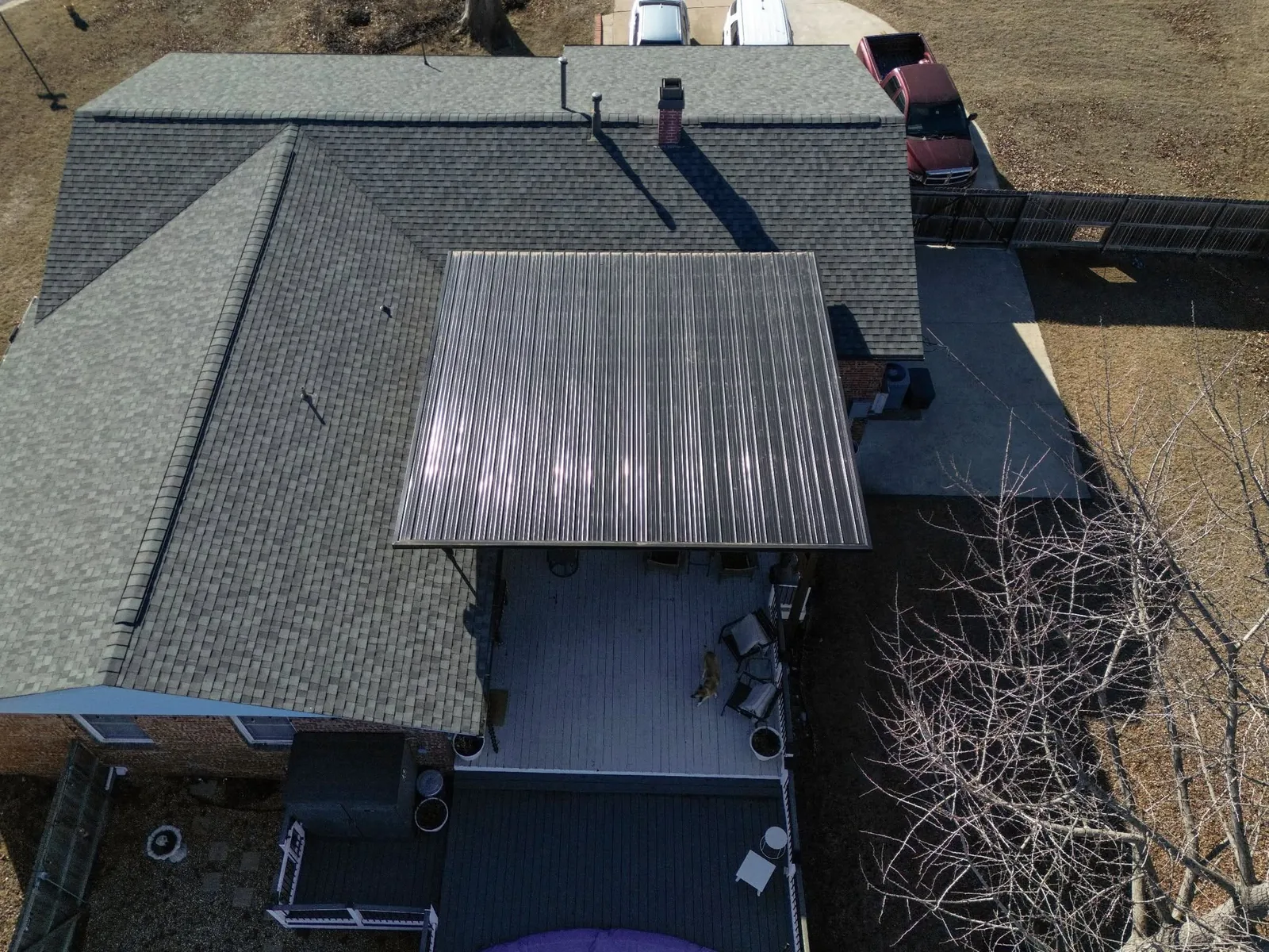An aerial view shows a house with a metal-roofed patio, a deck, and a dog on the deck.