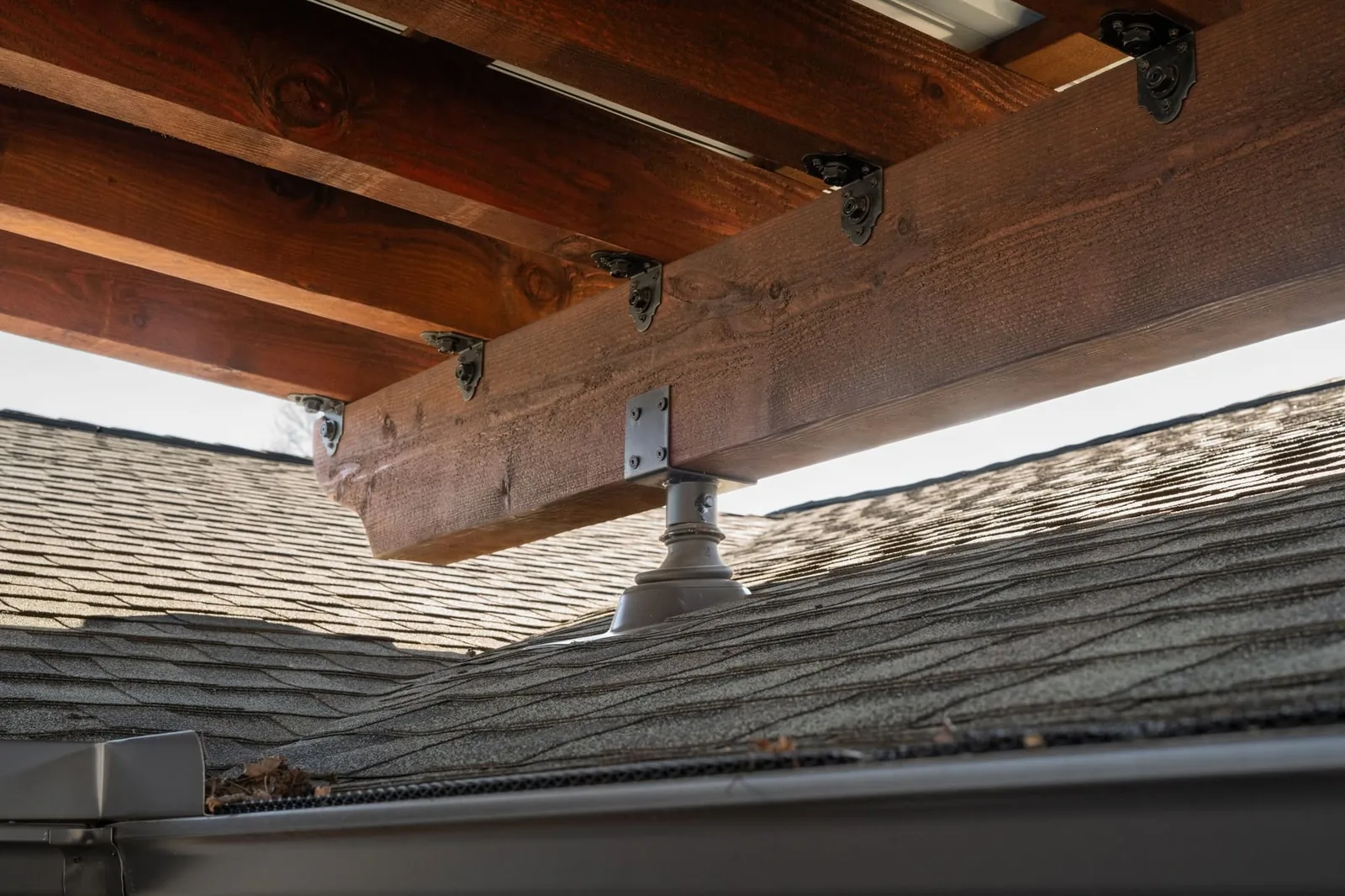 A wooden structure is supported by a metal post on a shingled roof.