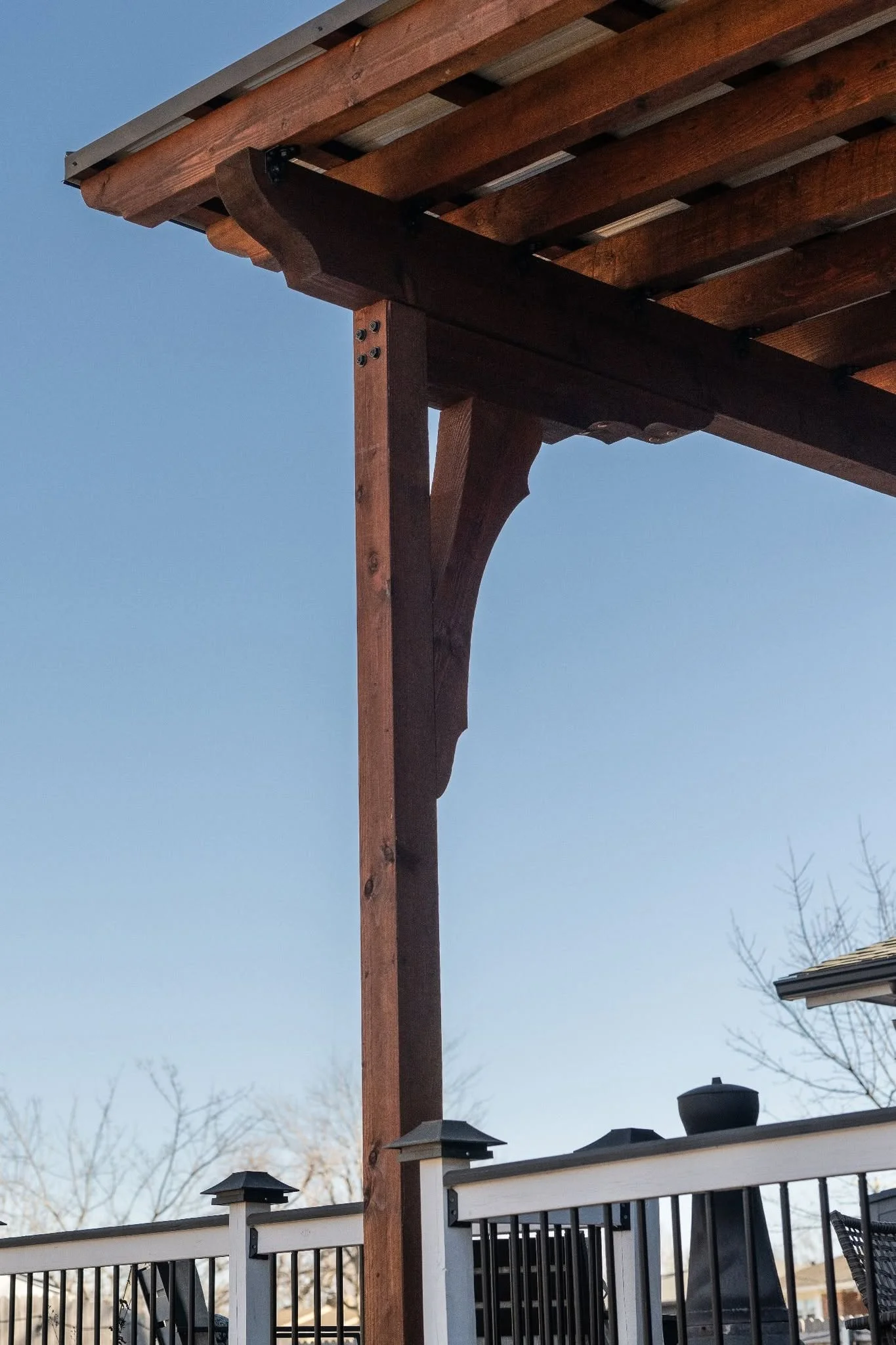A wooden pergola stands over a deck with a clear blue sky.