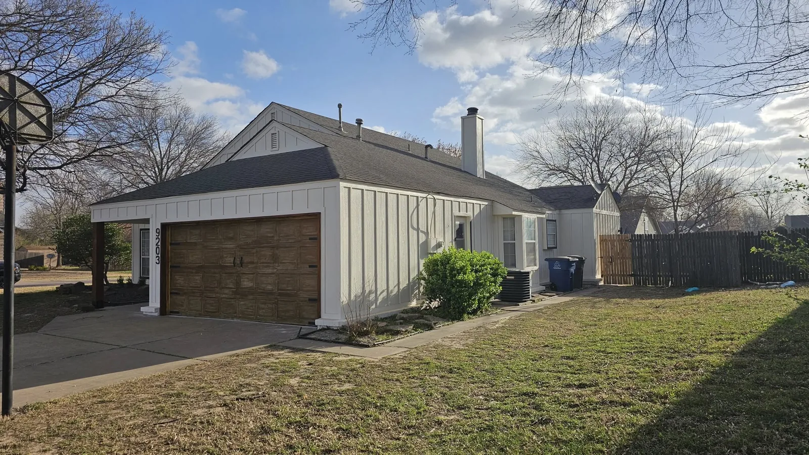 A white house with a brown garage door is shown in a suburban yard on a sunny day.