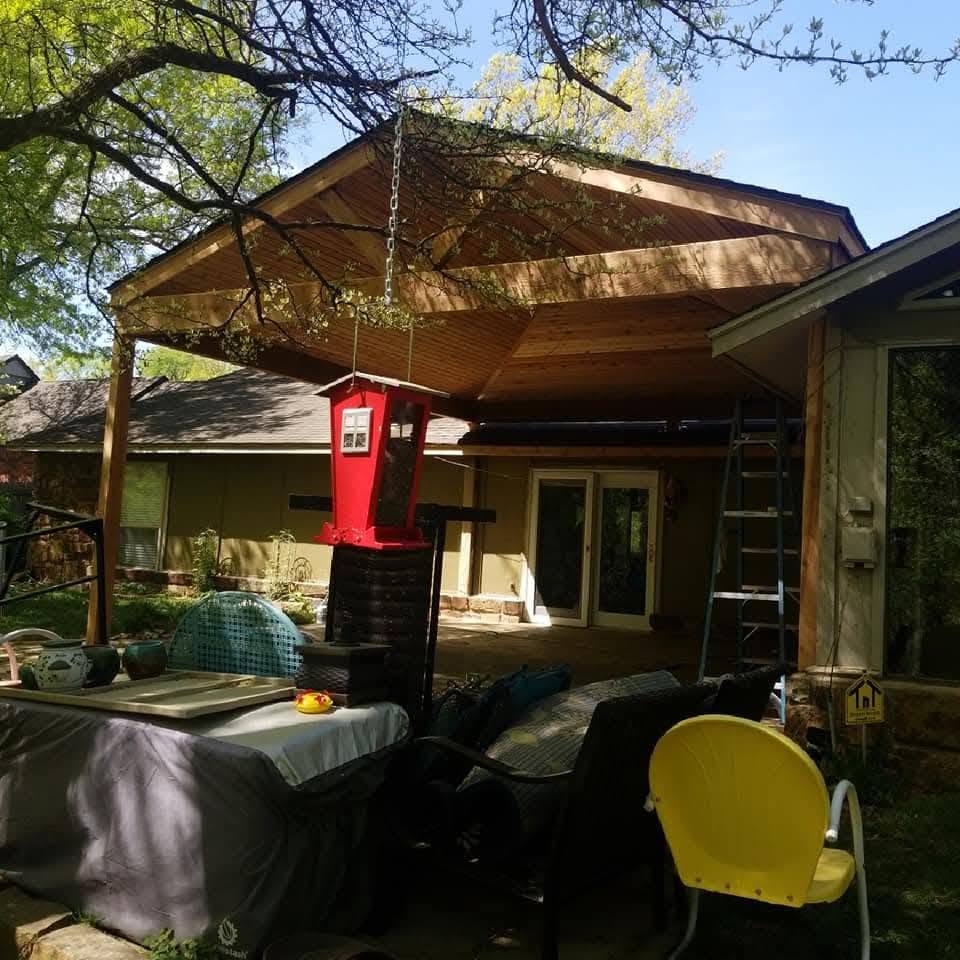 A red bird feeder hangs from a wooden patio cover in a backyard.