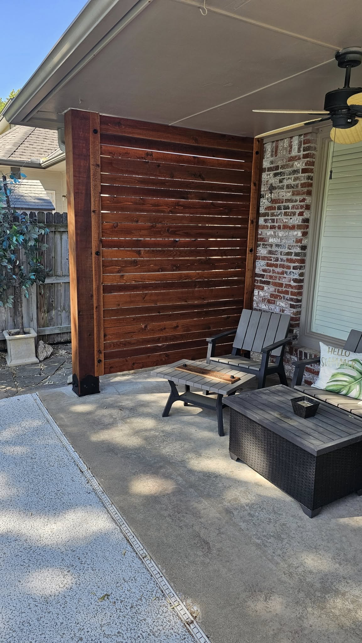 An outdoor patio with furniture, a wooden privacy screen, and a ceiling fan is shown.