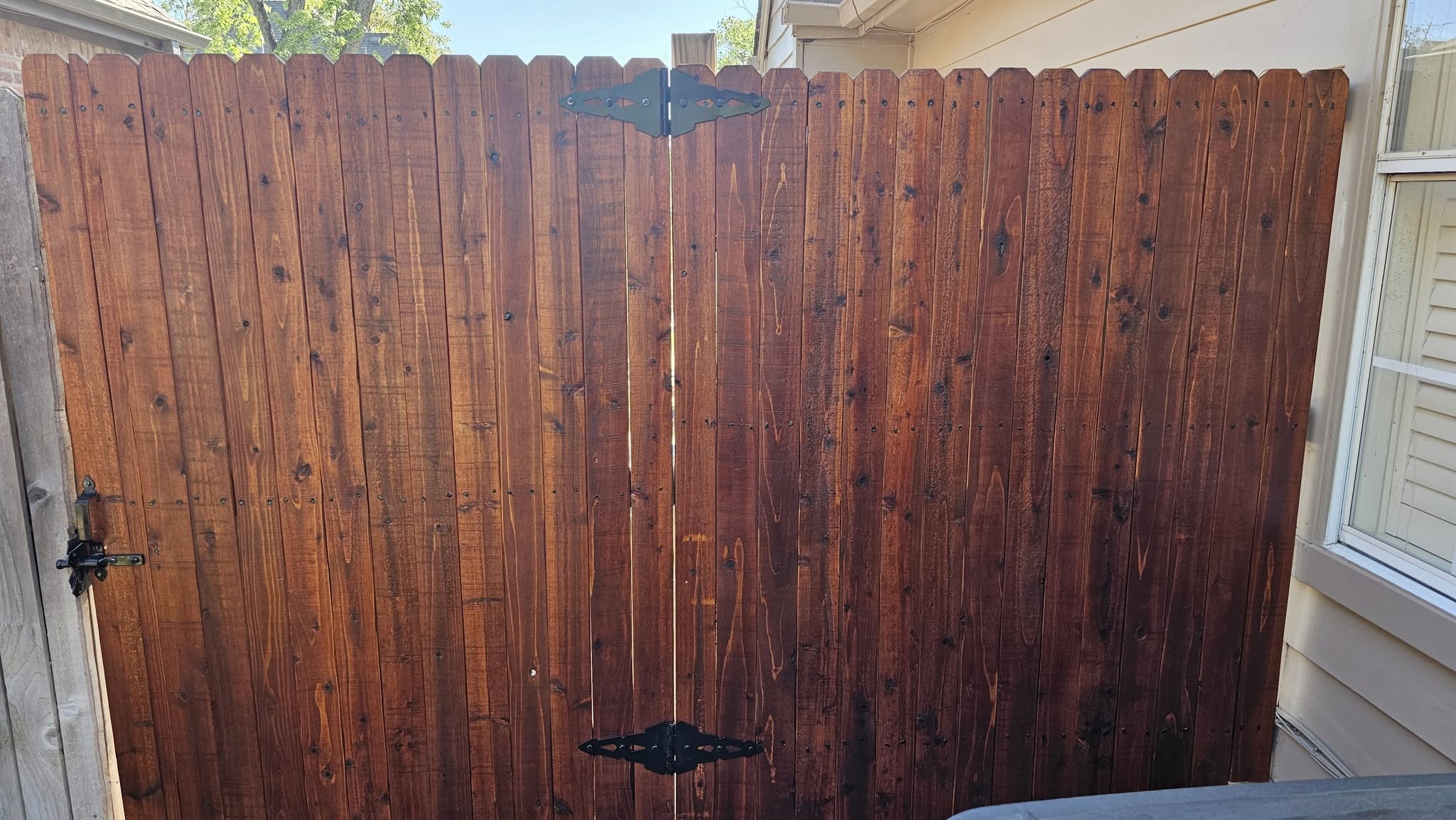 A wooden gate with black hardware stands against a beige house.