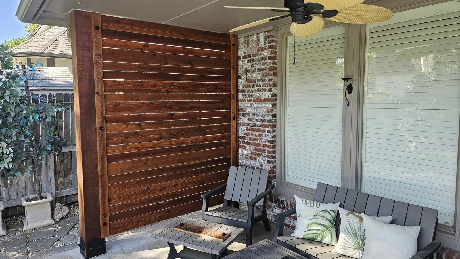 An outdoor patio with furniture, a wooden privacy screen, and a ceiling fan.