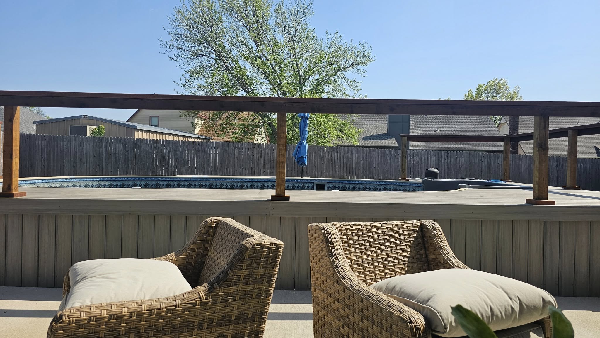 Two wicker chairs with cushions face a backyard pool and deck on a sunny day.