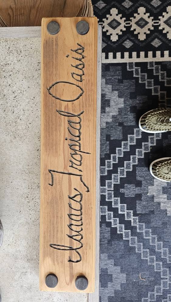 A wooden sign with "Isaac's Tropical Oasis" carved into it, placed on a rug.