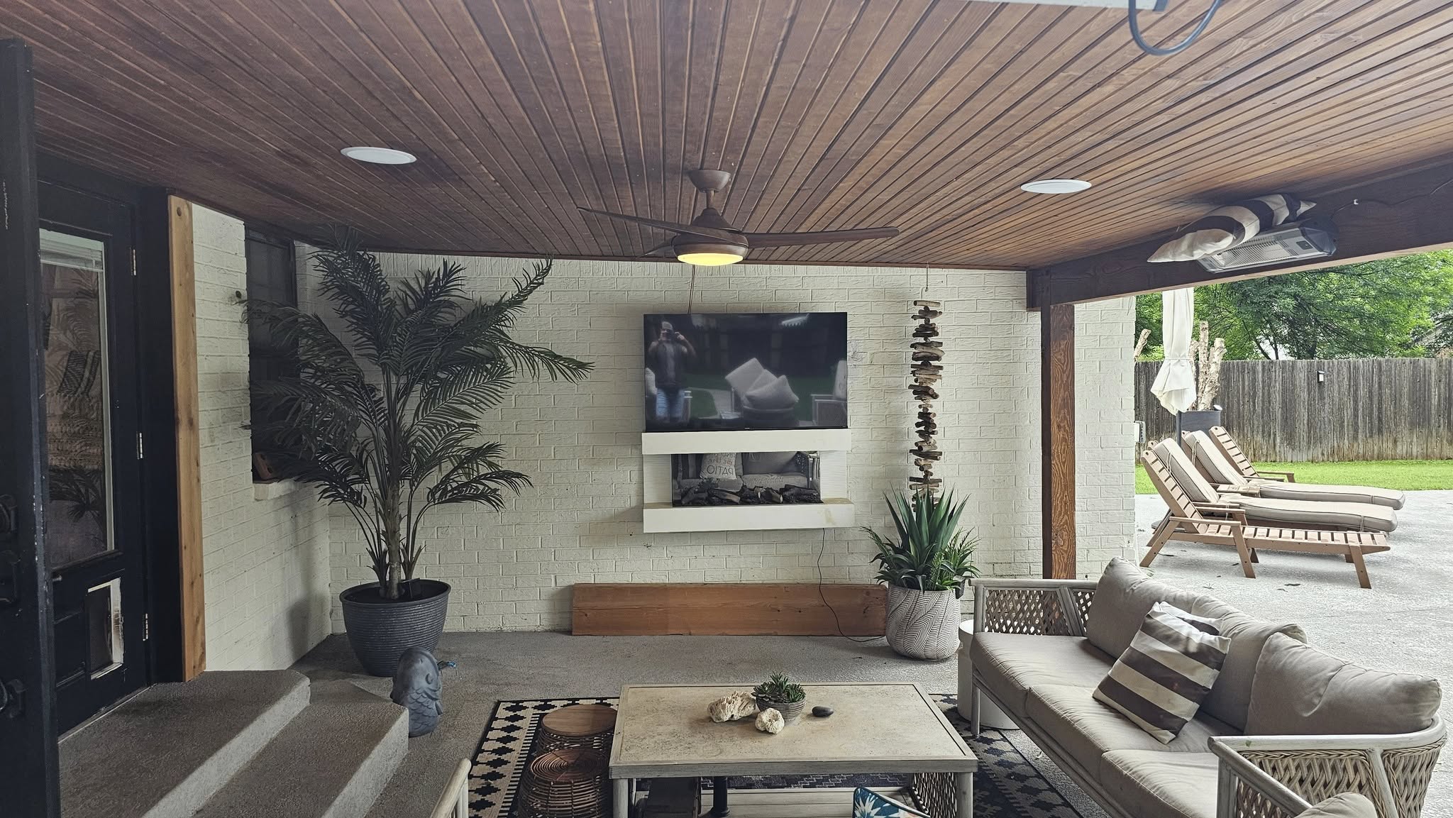 An outdoor patio with a TV, fireplace, seating, and lounge chairs.