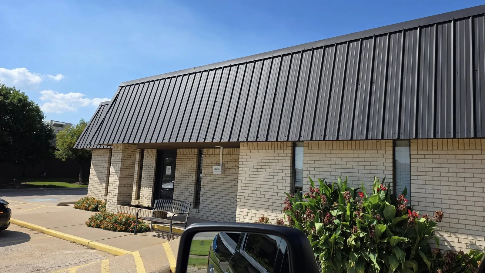 A brick building with a dark metal roof is shown outdoors on a sunny day.