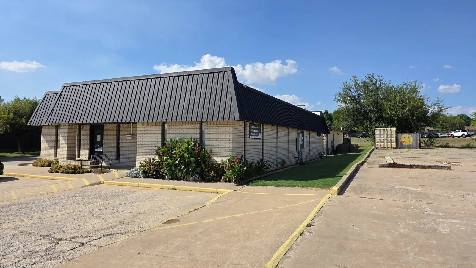 A brick building with a metal roof and a parking lot is shown.