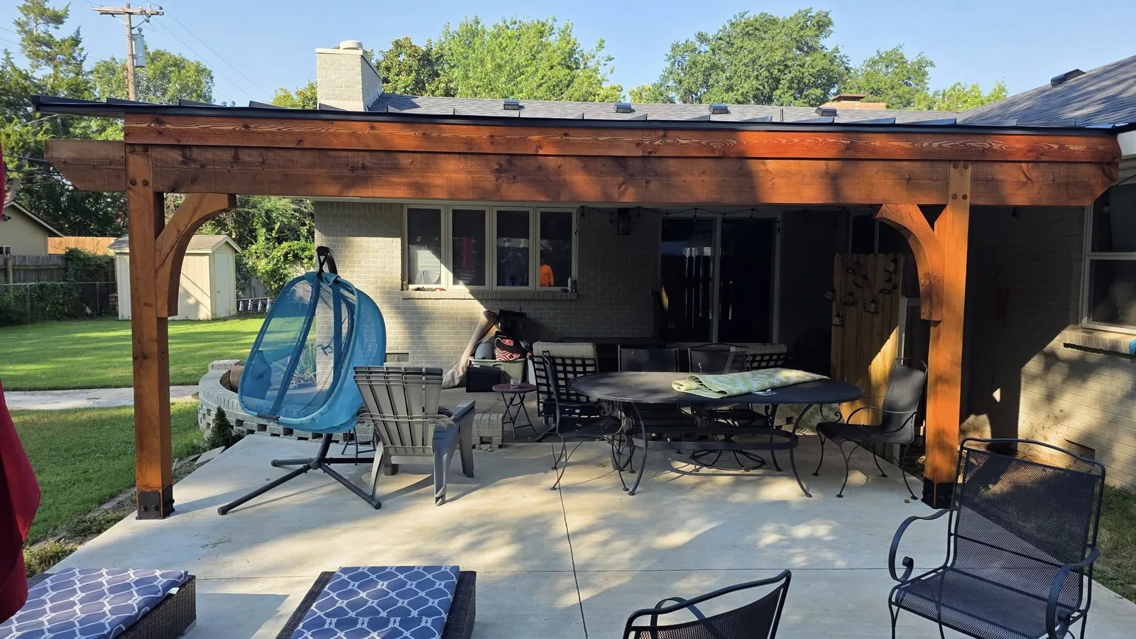 A covered patio with furniture and a hanging chair in a backyard.