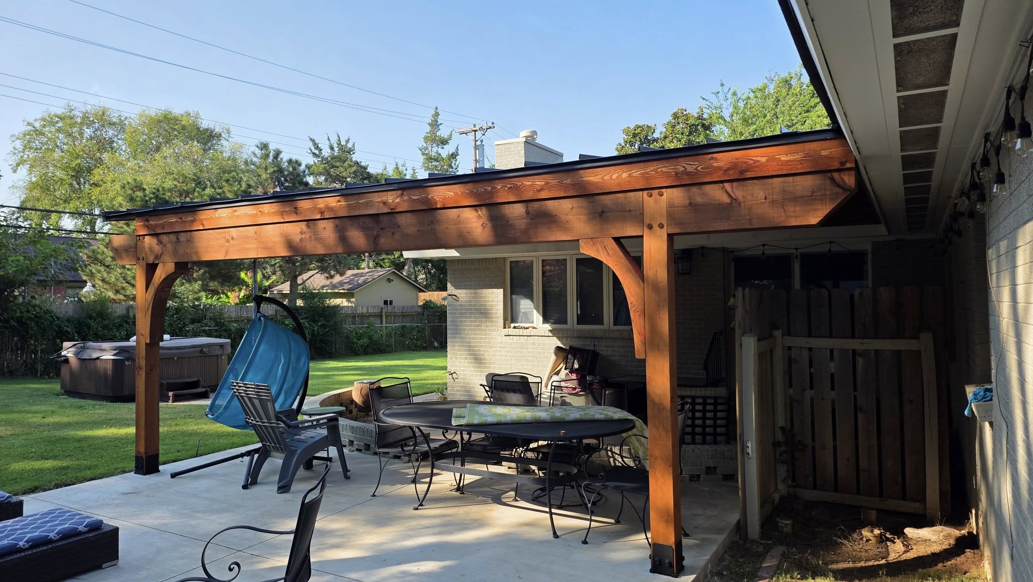 A backyard patio with a pergola, furniture, and a hot tub.
