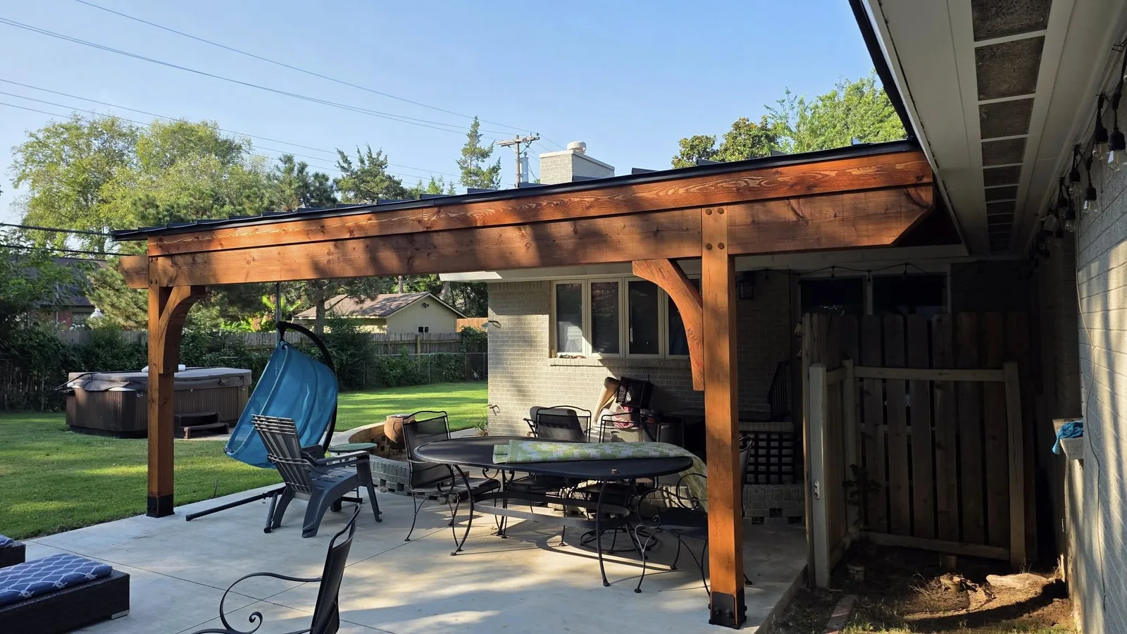 A backyard patio with a pergola, furniture, and a hot tub.