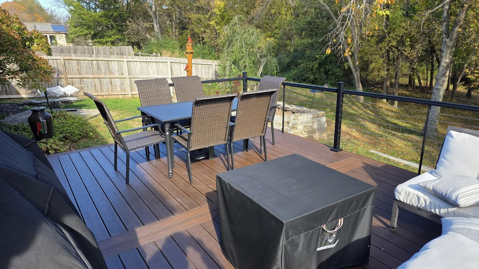 A backyard deck with a dining set, fire pit cover, and seating area.