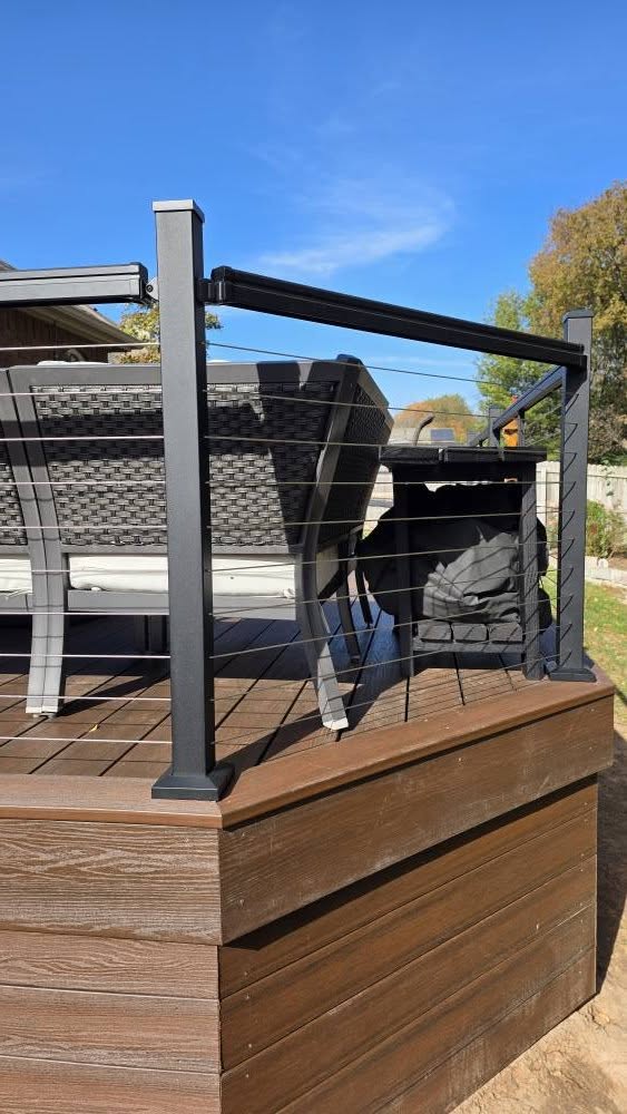 A modern deck with cable railings and outdoor furniture is shown on a sunny day.