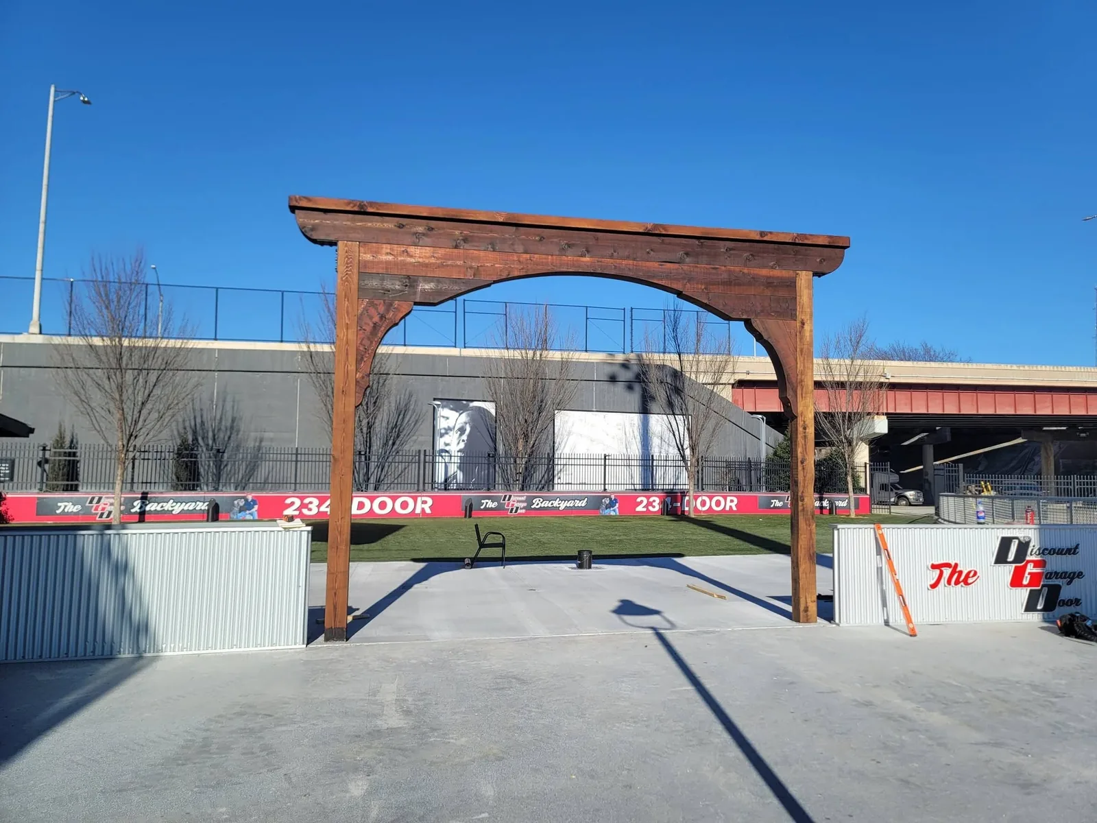 A wooden archway stands in an outdoor area with a clear blue sky.