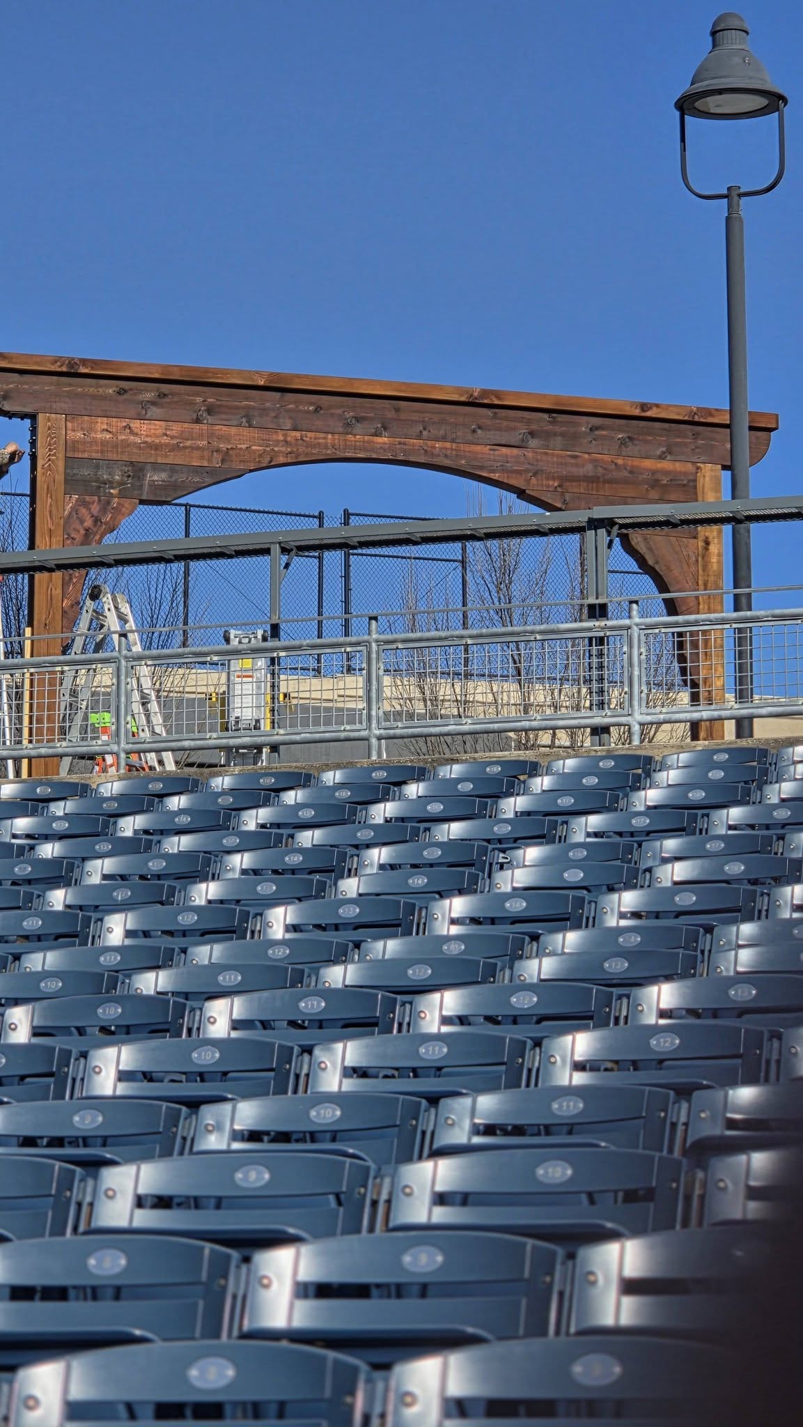 Empty stadium seats are in the foreground, with a wooden arch and a lamppost in the background.
