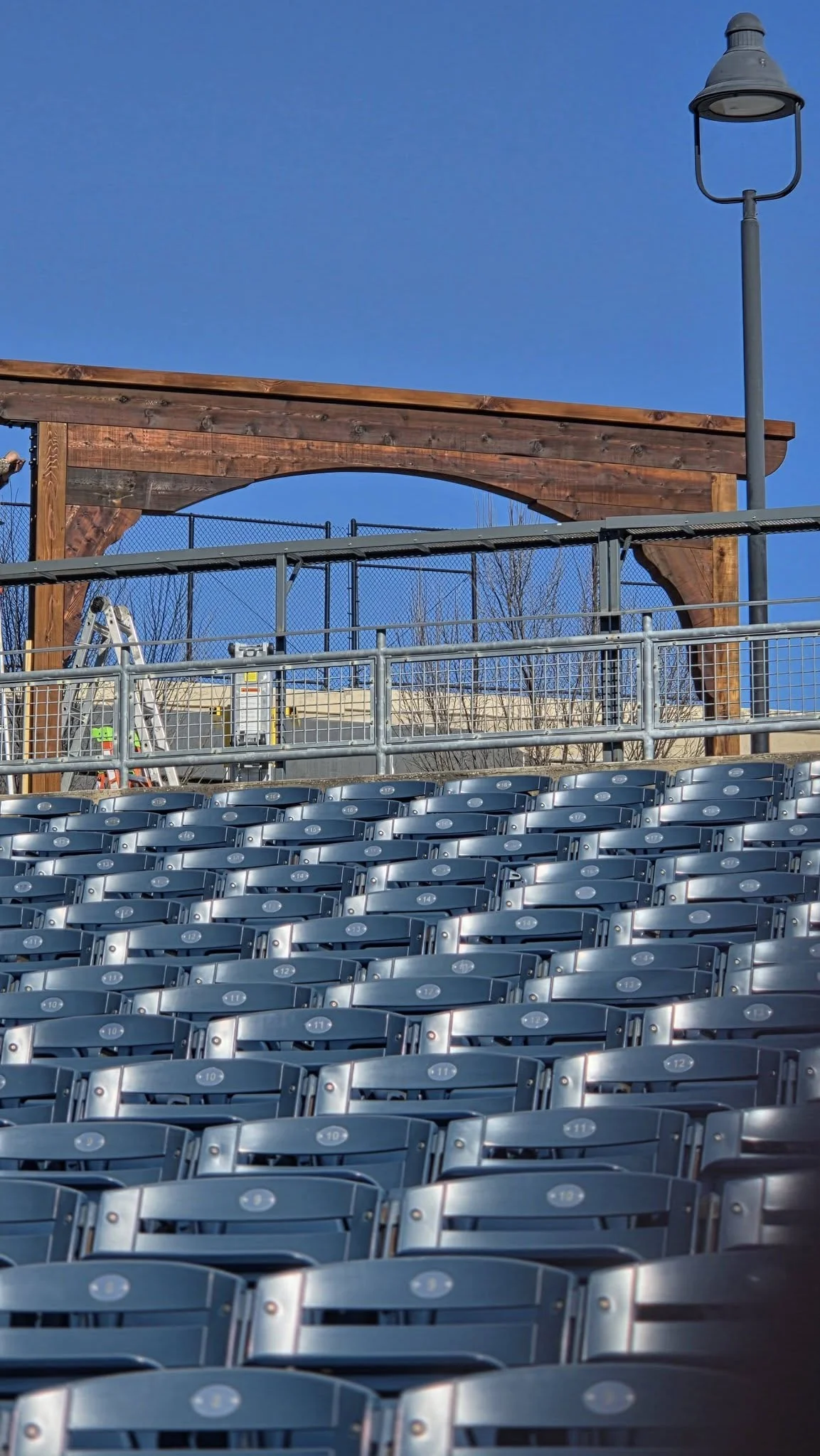 Empty stadium seats are in the foreground, with a wooden arch and a lamppost in the background.