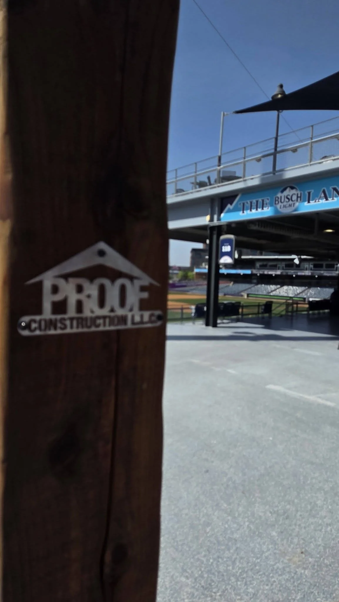 A sign for Proof Construction LLC is on a wooden post in front of a stadium.
