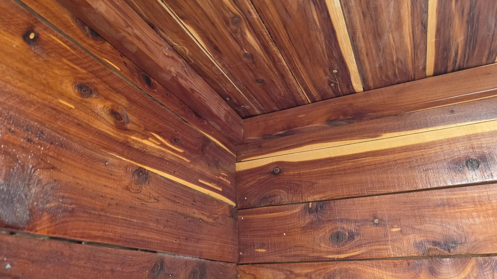 A corner of a wooden structure with reddish-brown planks and knots.
