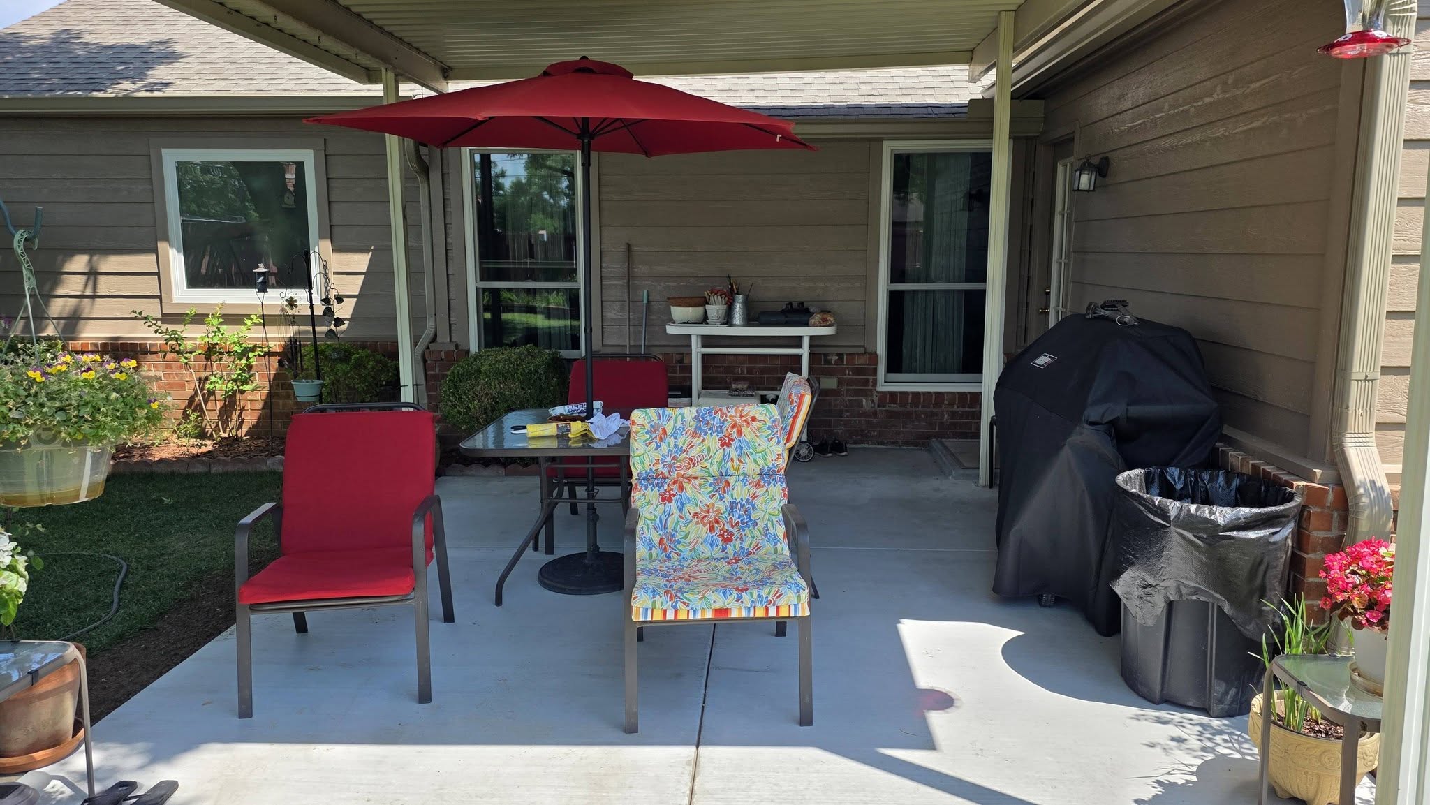 A covered patio with a grill, trash can, table, chairs, and umbrella.