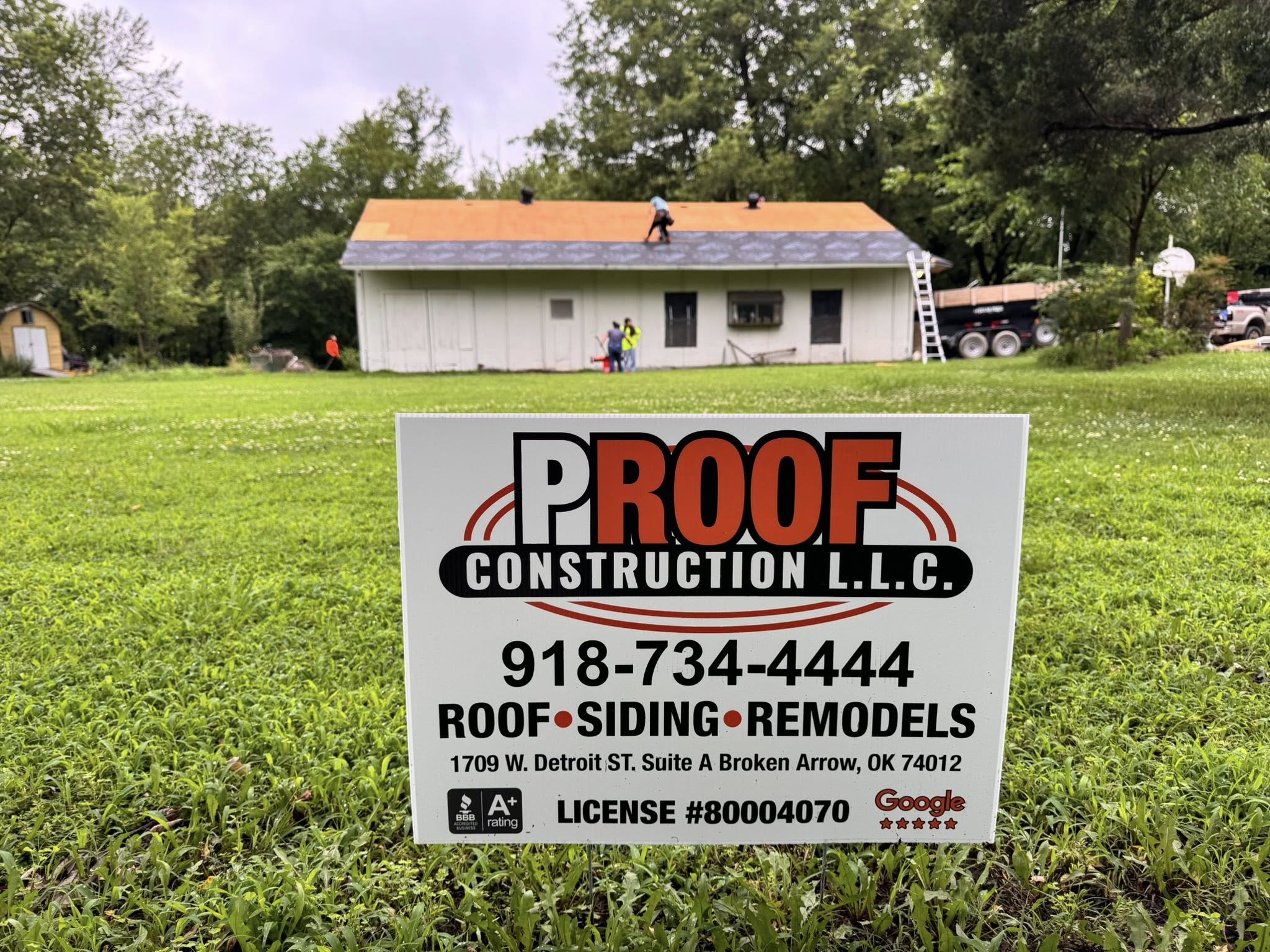 Roofers work on a house while a sign for Proof Construction LLC is in the foreground.