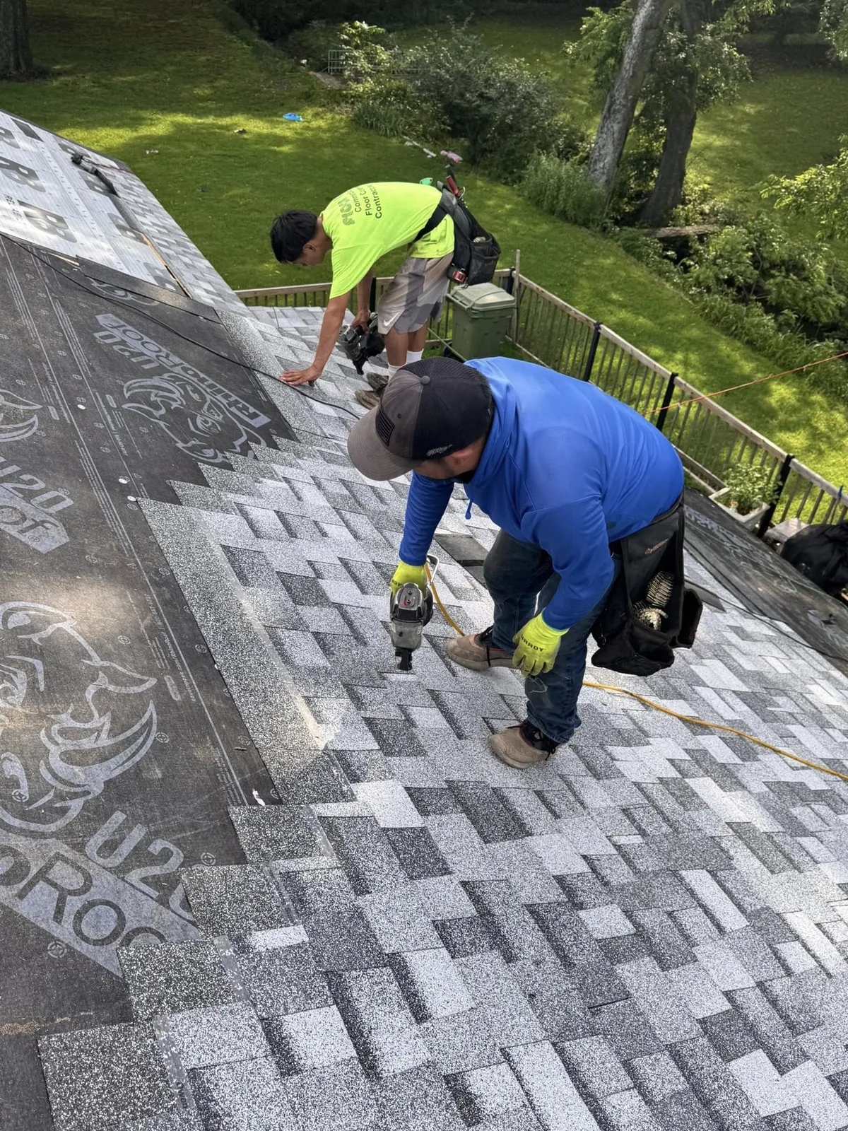 Two roofers install shingles on a house roof.