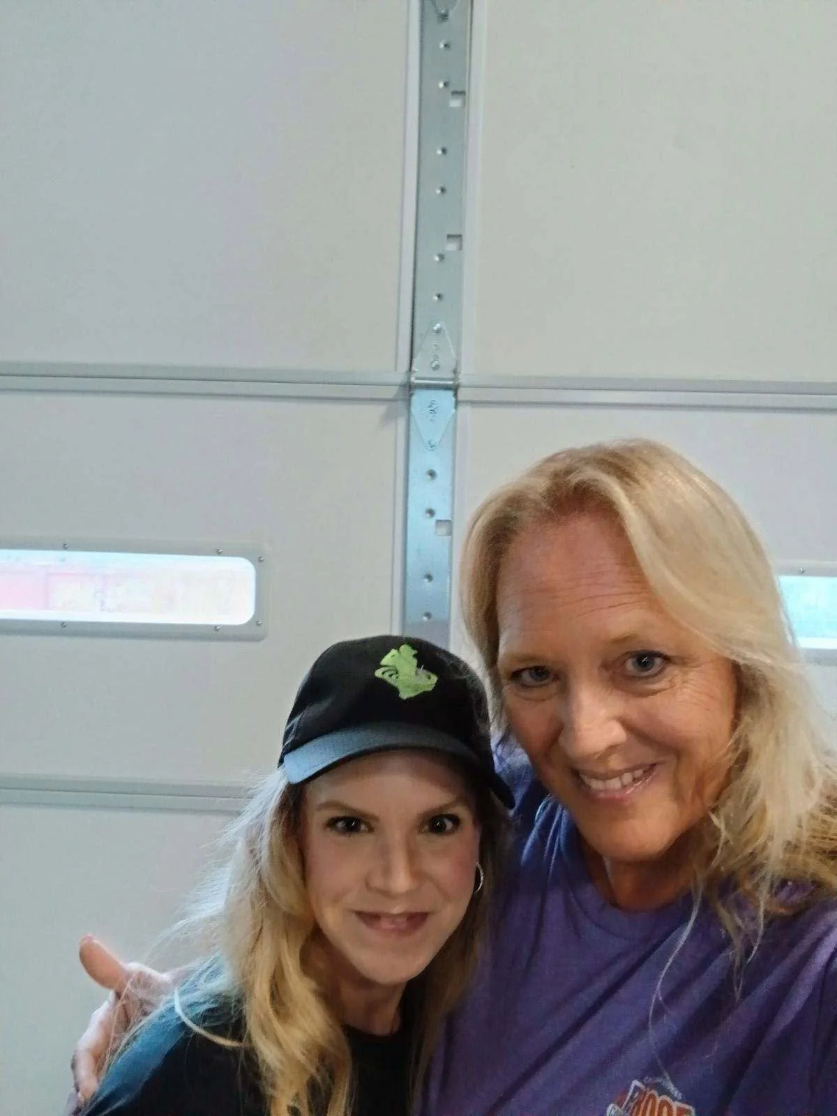 Two women smile for a selfie in front of a garage door.